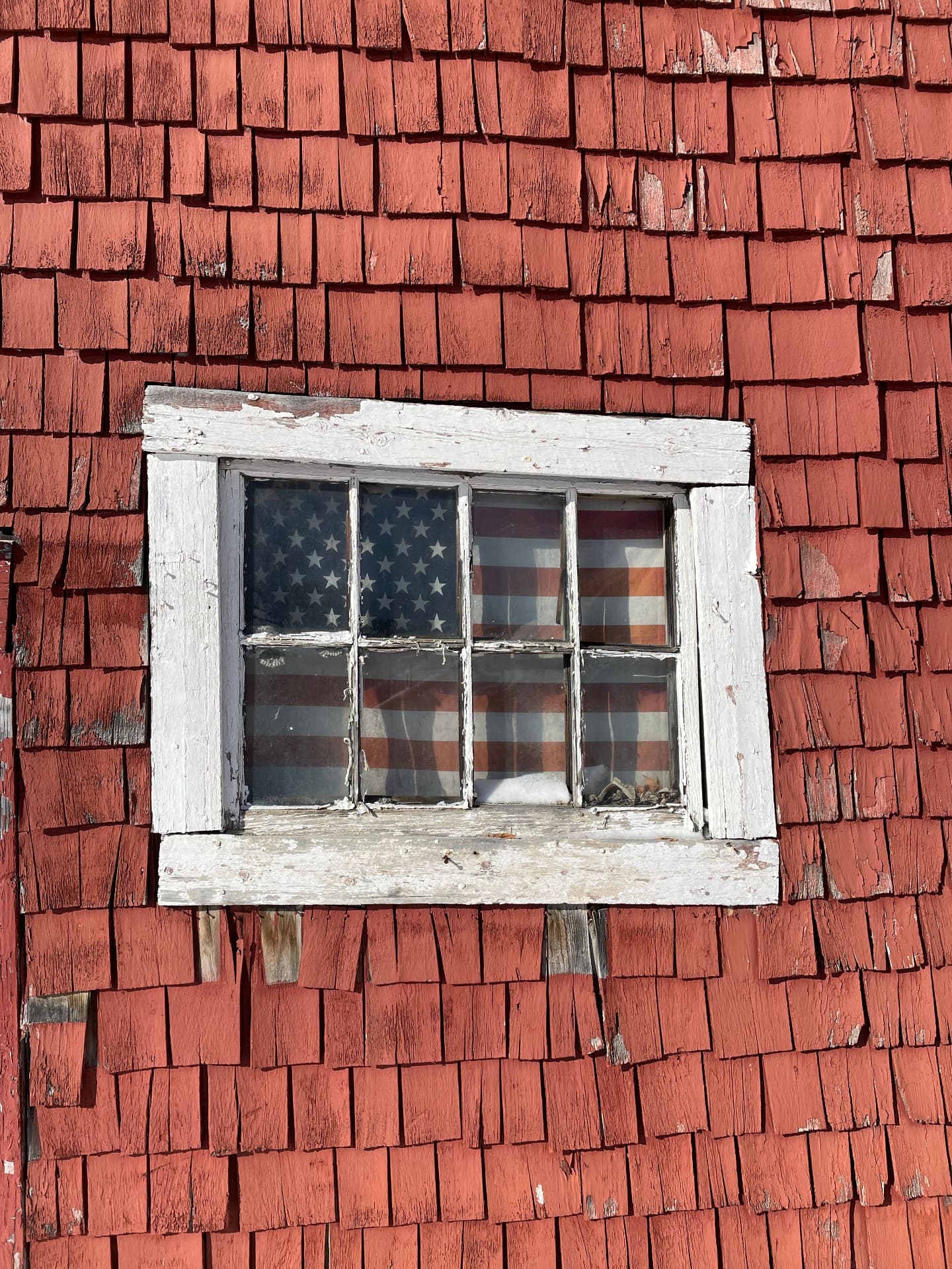 Weathered red shingles and an old window with a flag behind the glass